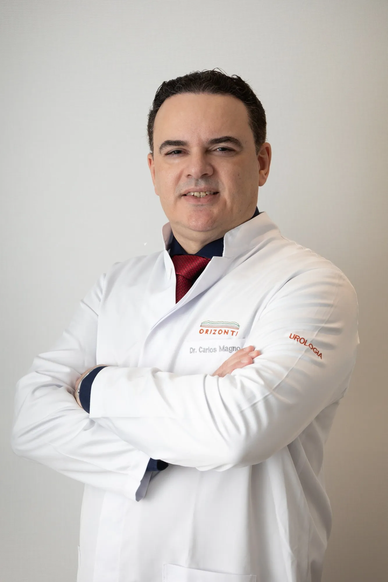Dr. Carlos Magno, urologista, de jaleco e braços cruzados, sorrindo