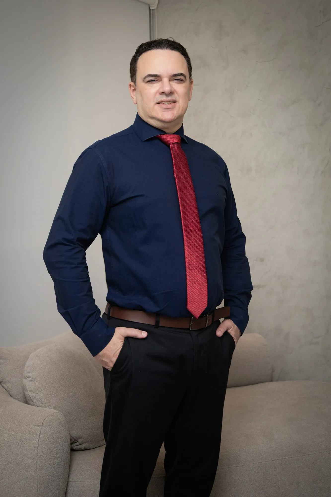 Dr. Carlos Magno de camisa azul e gravata vermelha, com a mão no bolso
